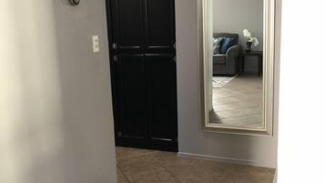 A hallway with a black door, a white wall, and a tiled floor.