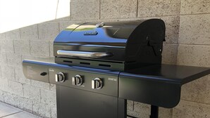 Una parrilla portátil para barbacoa con pantalla digital, repisa lateral y mesa plegable.