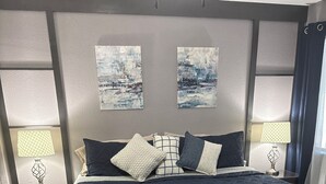 Una cama bien tendida con un edredón azul oscuro, dos lámparas de noche y una mesita de noche con una lámpara.