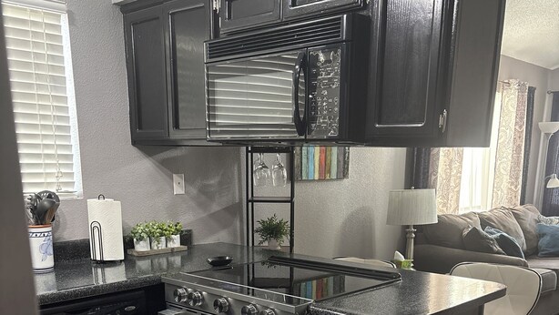 Una cocina compacta con armarios oscuros, horno empotrado y placa de cocina.