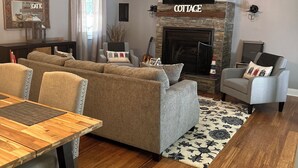 A spacious living room with a fireplace, a ceiling fan, and a dining area with a wooden table and chairs. - Pier Joy: Two private cottages on 2.5 wooded acres, close to Union Pier beaches (Union Pier)