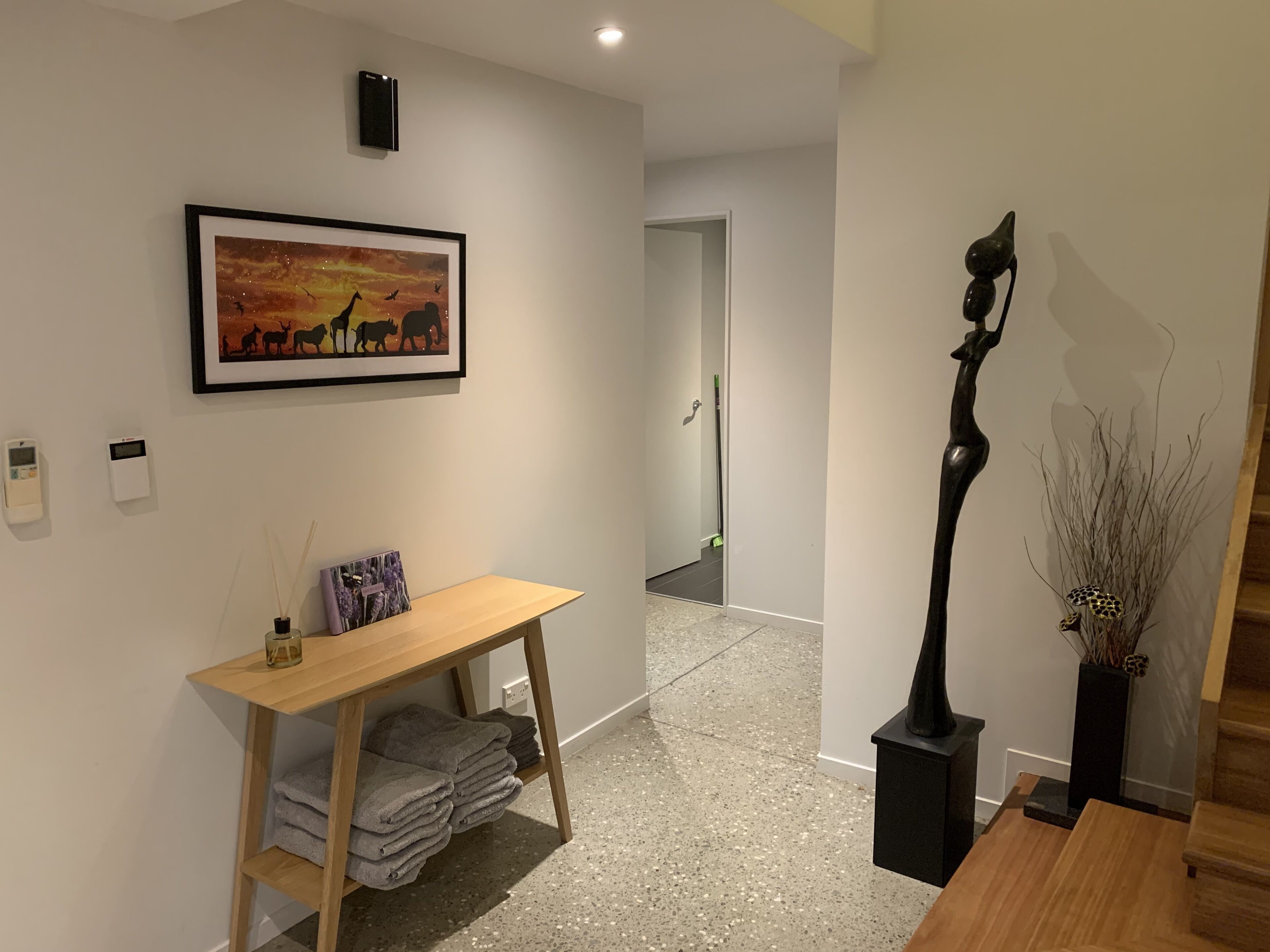 A modern interior with a wooden desk, a framed painting, a sculpture, and a vase with branches.
