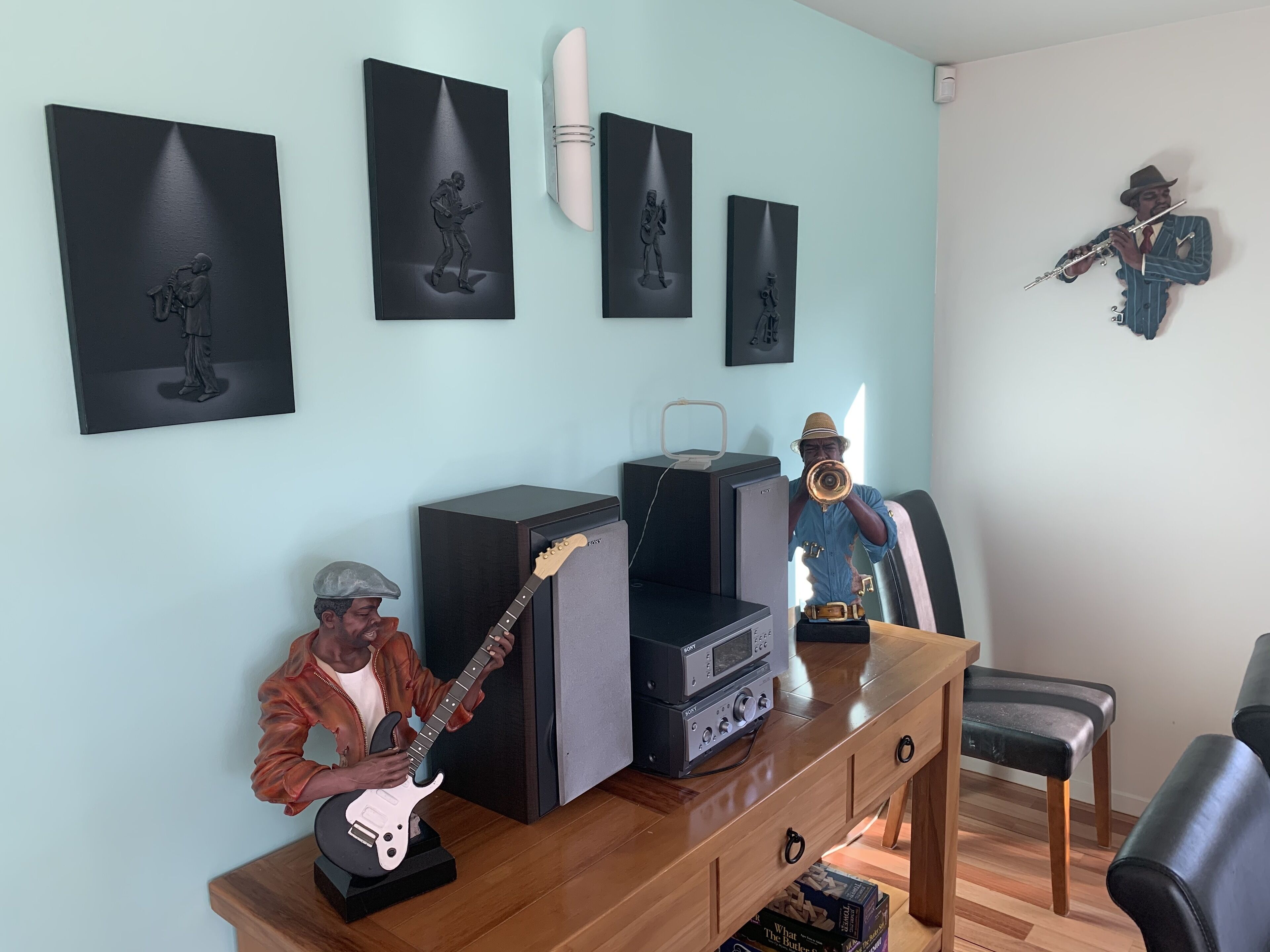 Ett rum med ett skrivbord i trä, en gitarr, en stereoanläggning och en staty av en man som spelar trumpet.
