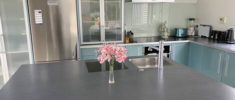 A modern kitchen with a stainless steel refrigerator, a glass-fronted cabinet, a sink, and a vase with flowers on the countertop.