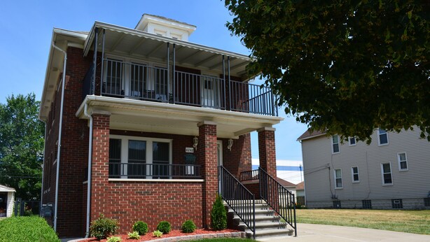 A two-story brick building with a balcony, a front entrance, and a small front yard with plants. - HomeAway Residential Apartment (Dearborn)