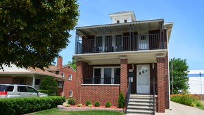 A two-story brick building with a balcony, a front door, and a small front yard with a hedge and a few plants. - HomeAway Residential Apartment (Dearborn)