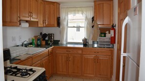 A kitchen with wooden cabinets, a stove, a sink, and a window with curtains. - HomeAway Residential Apartment (Dearborn)