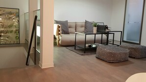 A modern living room with a sofa, ottomans, a glass coffee table, and a framed artwork on the wall.