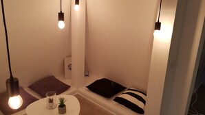 A small, cozy room with a round table, two potted plants, and a bench with cushions.