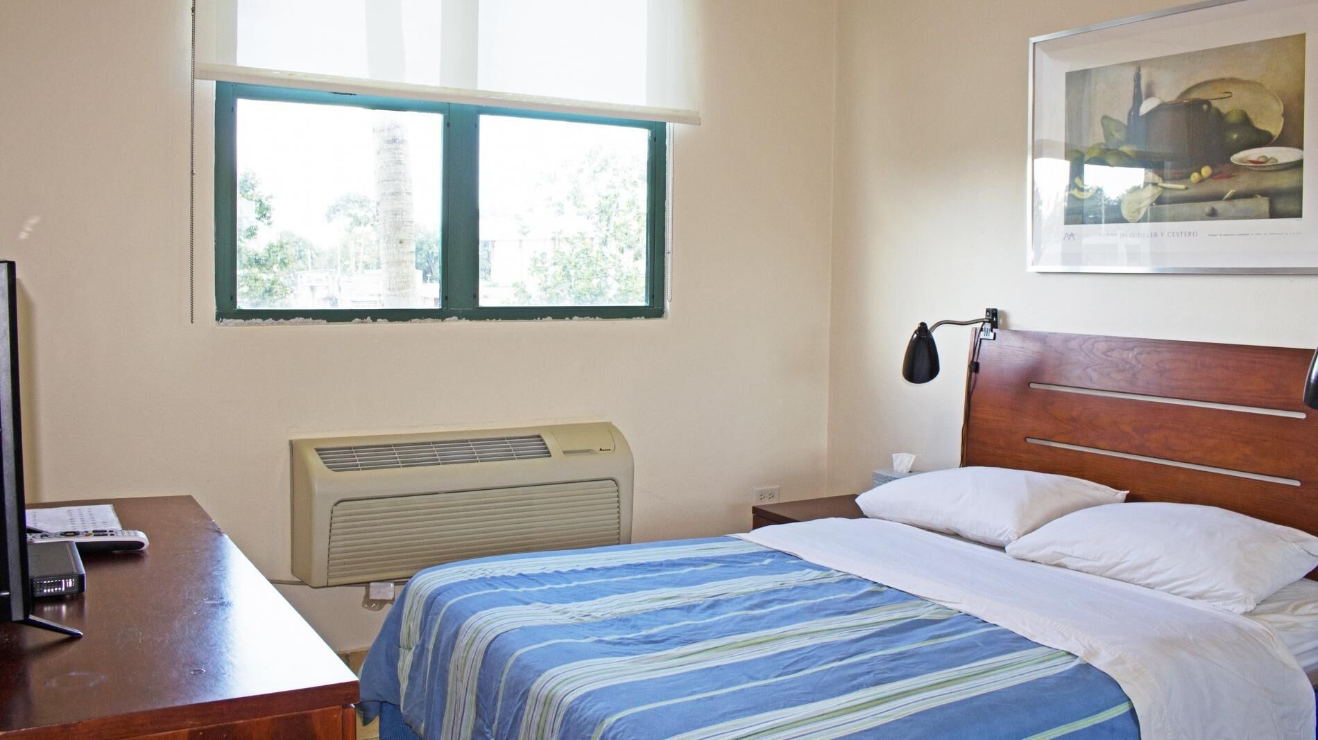 A bedroom with a bed, a desk with a computer, a window, and a radiator.