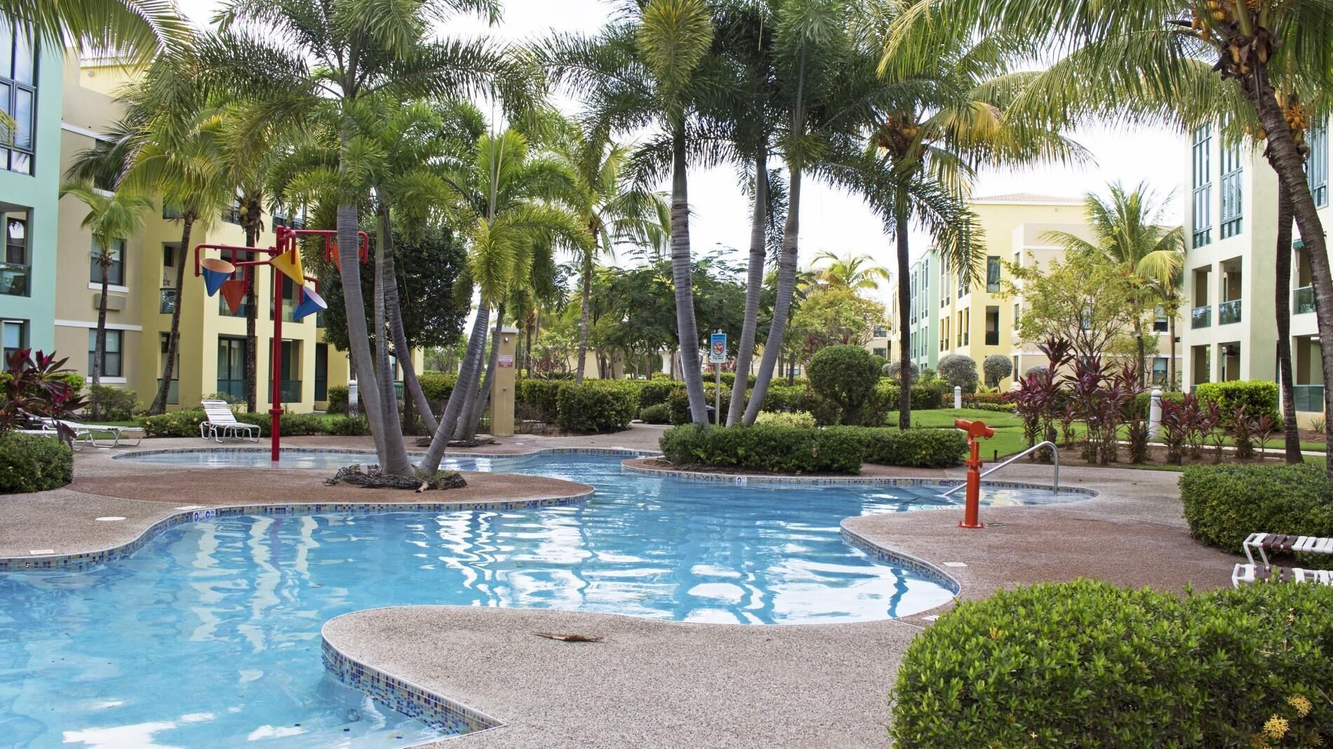 A pool surrounded by palm trees and a building with balconies.