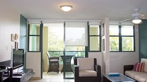 Una sala de estar con televisor, sofá, mesa de centro y balcón con sillas.