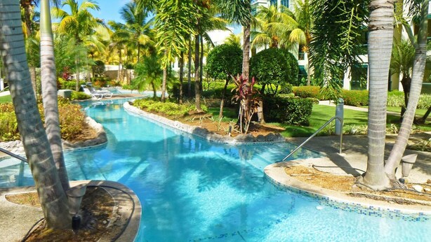 Una piscina de diseño curvo, rodeada de palmeras y jardines bien cuidados.