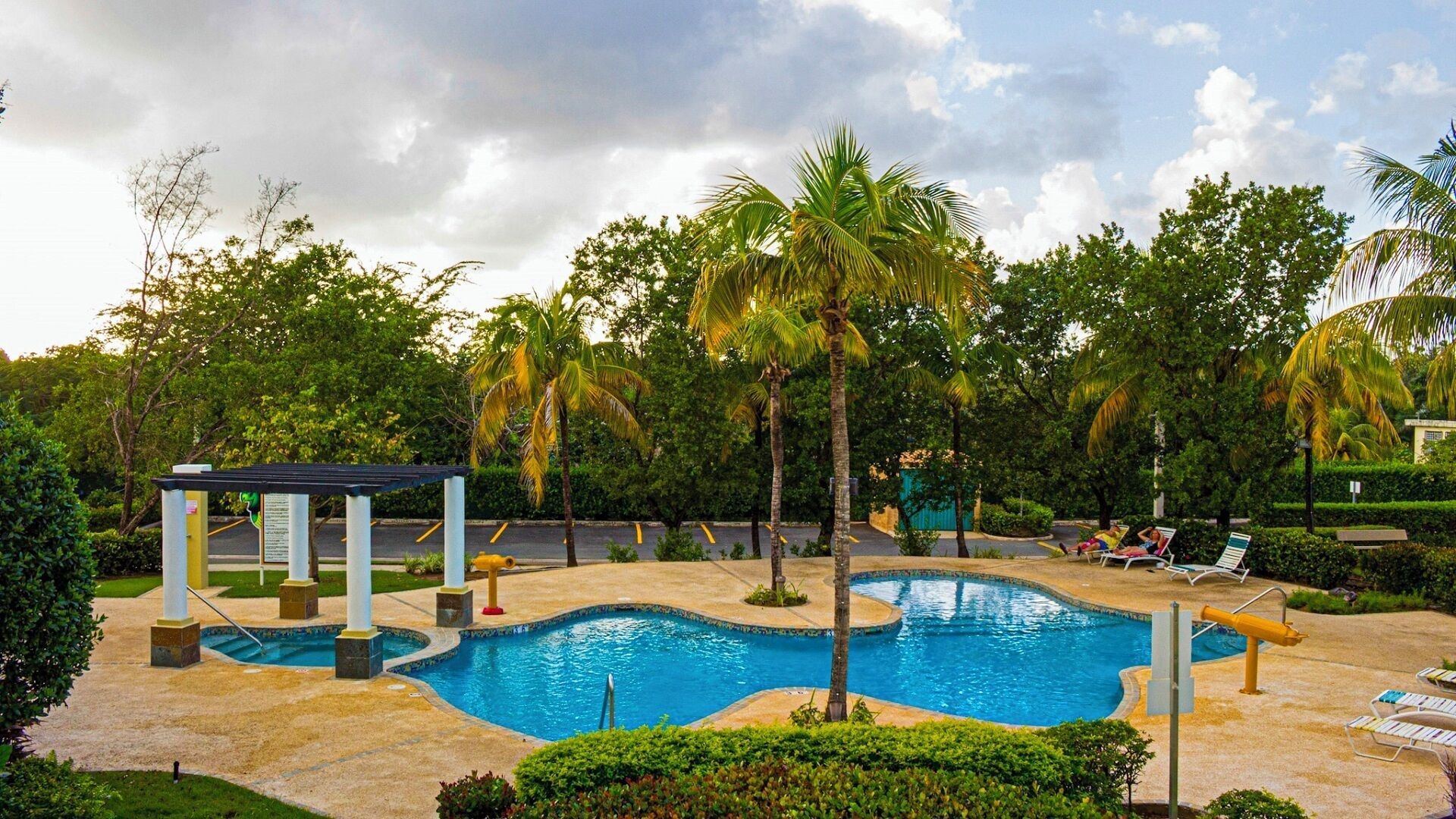 Una piscina con una terraza circundante, palmeras y sillas de descanso.