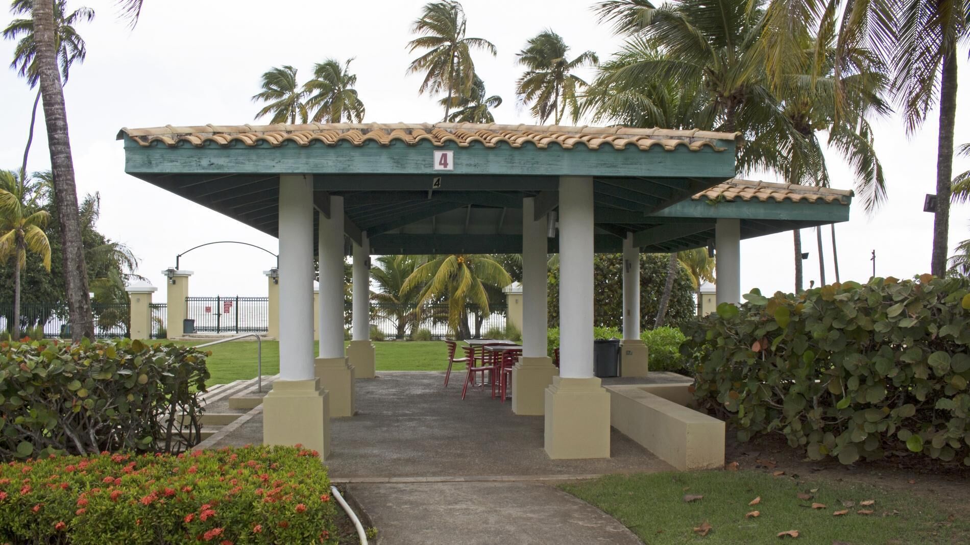 A covered outdoor seating area with a tiled roof, palm trees, and a sign indicating the number 4.