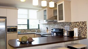 Una cocina moderna con gabinetes blancos, una estufa negra, un microondas y un lavamanos. Hay una ventana que proporciona luz natural y un cuenco decorativo sobre la encimera.