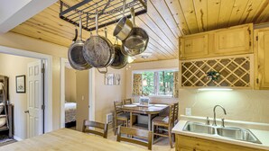 A wooden kitchen with hanging pots, a dining table, chairs, and a sink. - 4 Mi to Rainbow Lake! Cozy Forest-View Gem w/ Deck (Lakeside)