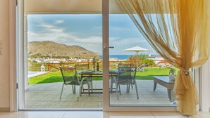 A room with a sliding glass door leading to an outdoor patio with a table and chairs, a view of a mountainous landscape, and a pool area. - Villa Balos with fantastic sea view (Chania)