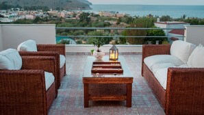 A balcony with wicker furniture, a glass table, and a view of the sea and town. - Villa Balos with fantastic sea view (Chania)