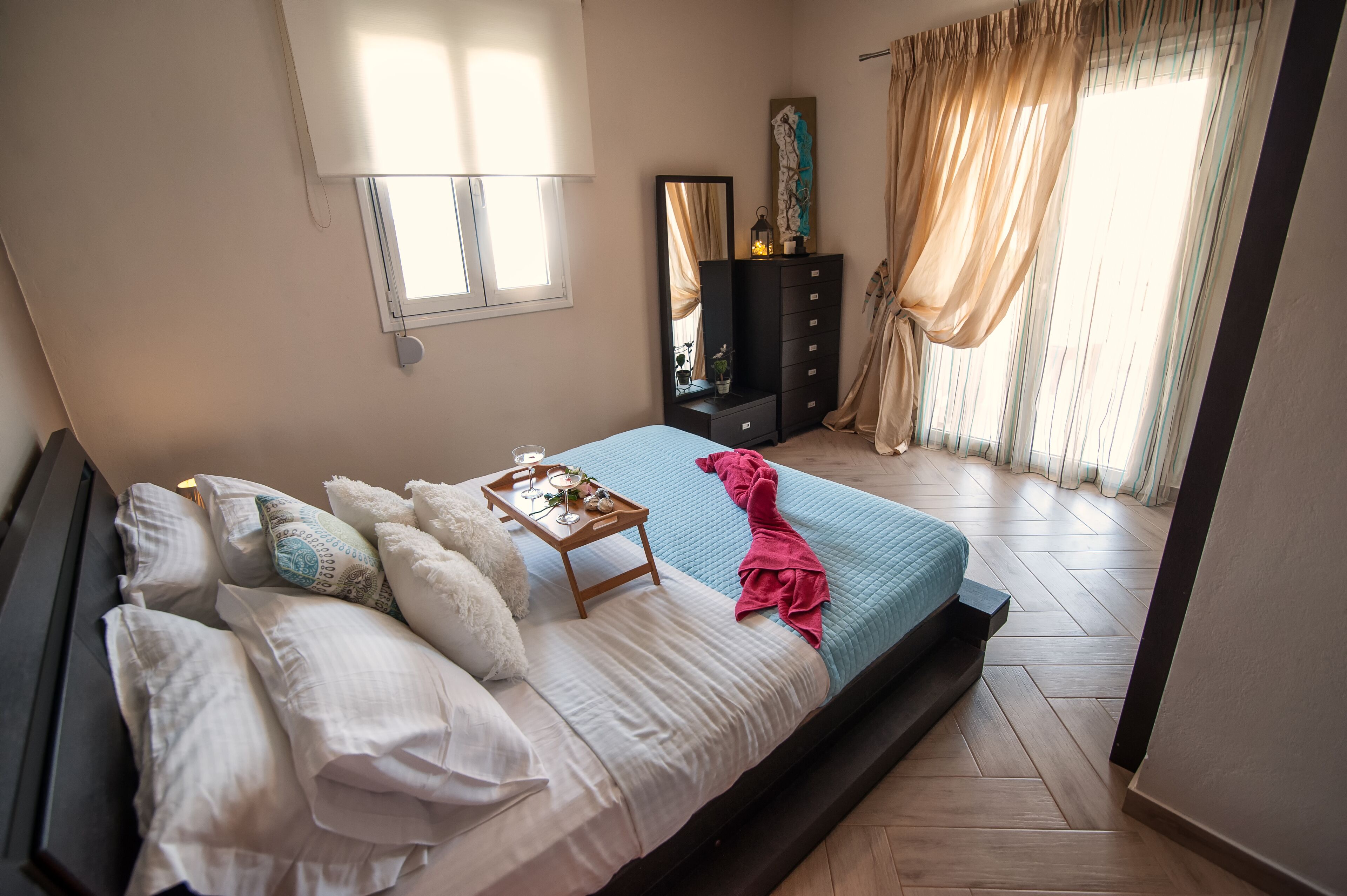 A bedroom with a bed, a dresser, a mirror, and a window with curtains.