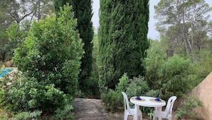 A stone pathway leading to a white round table with four chairs, surrounded by lush greenery and tall trees. - Villa with a 12.5 metre swimming-pool, not far from the sea (Puget-sur-Argens)
