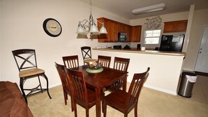 Un comedor con mesa y sillas de madera, una araña y una cocina al fondo.