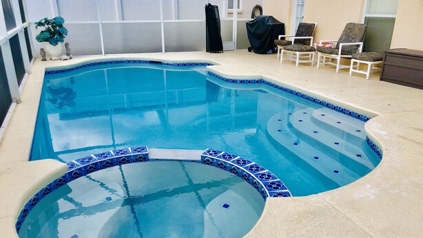 Une piscine au design incurvé, avec un bord en carrelage bleu.