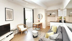 A modern living room with a flat-screen TV, a sofa, a dining table, and a wicker chair. - Stunning, Upmarket and Newly furnished Apartment nearby all Major Attractions (Antibes)