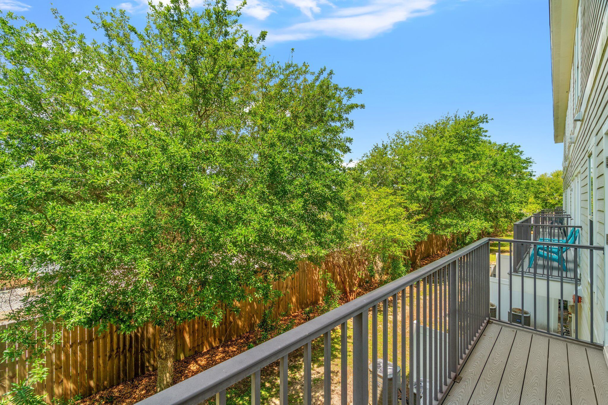 A wooden deck with a metal railing, surrounded by lush green trees.