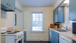 A compact kitchen with a stove, oven, and dishwasher, light blue cabinets, and a window providing natural light. - This cottage is a 1 bedroom(s), 1.5 bathrooms, located in Manchester, VT. (Manchester)