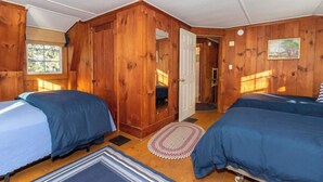 A room with two beds, wooden walls, a door leading to another room, and a window. - This cottage is a 1 bedroom(s), 1.5 bathrooms, located in Manchester, VT. (Manchester)