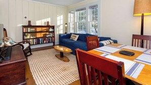 A cozy living room with a blue sofa, a wooden coffee table, a bookshelf, and a dining table with placemats. - This cottage is a 1 bedroom(s), 1.5 bathrooms, located in Manchester, VT. (Manchester)