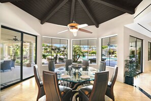 A dining area with a glass table, leather chairs, and a ceiling fan.