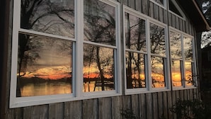 Een houten hut met grote ramen die een zonsondergang weerspiegelen.