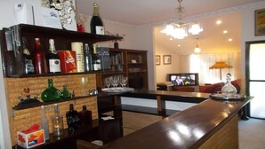 A bar area with shelves of liquor bottles and glasses, a television in the background, and a chandelier.