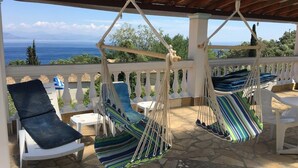 A covered outdoor seating area with two hanging hammocks and a white chair. - Romantic sea view Studio for two (Corfu)