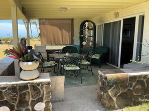 A covered patio with a table and chairs, a stone wall, and a view of the ocean.