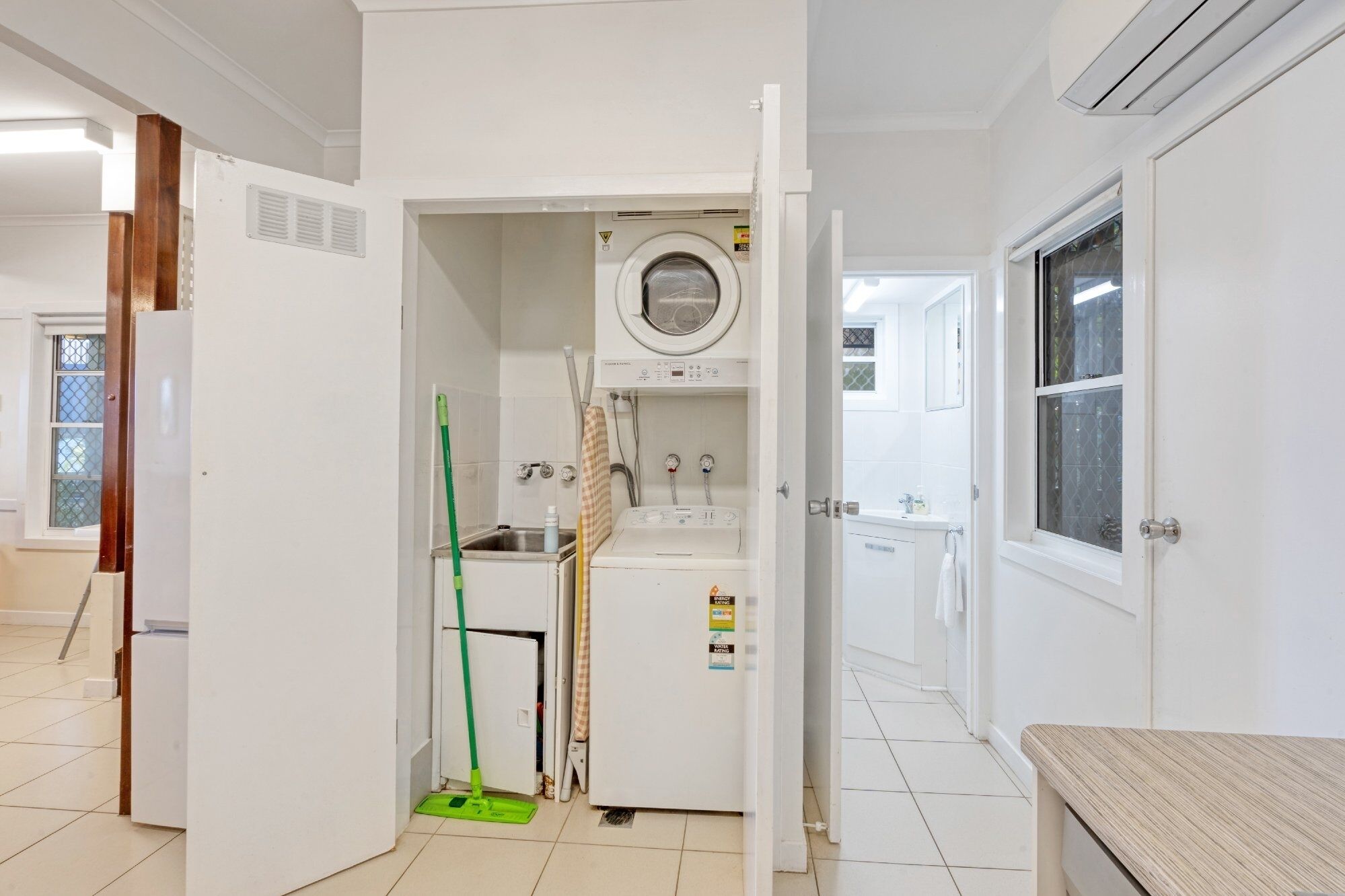 A compact, well-lit bathroom with a washing machine, a sink, and a mop.