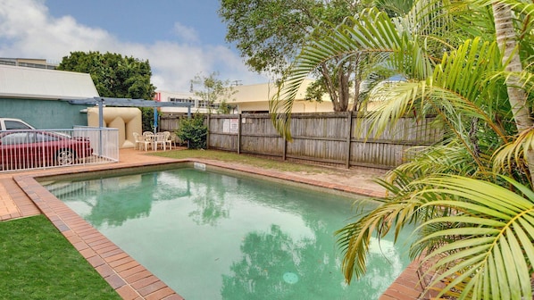 A rectangular swimming pool with a brick border, surrounded by a wooden fence and lush greenery. - Location, location, location! for this 2 Bedroom apartment in the middle of everything (Mooloolaba)