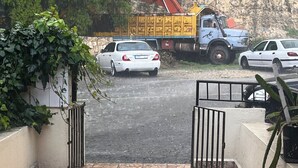 A paved entrance with a metal gate, a white car parked in the background, and a yellow construction vehicle.