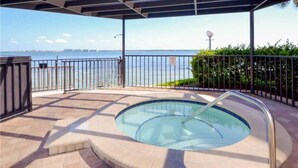 A hot tub with a view of the water, surrounded by a metal fence and a covered area with a roof.