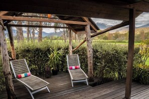 A wooden deck with two lounge chairs, a pergola, and a view of a green landscape with trees and mountains.