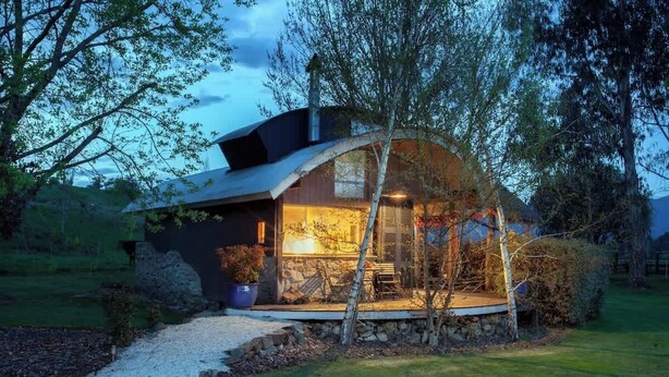 Ein modernes Haus mit Natursteinaußenwand, einer Veranda und einem gepflegten Garten.