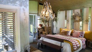 Ein Schlafzimmer mit einem Bett, einer Bank, einem Chandelier und einem Fenster mit Jalousien.