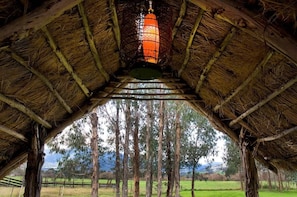 Una struttura con tetto di paglia, un lampadario appeso, una scala che conduce a un'area aperta con alberi e vista sul paesaggio.