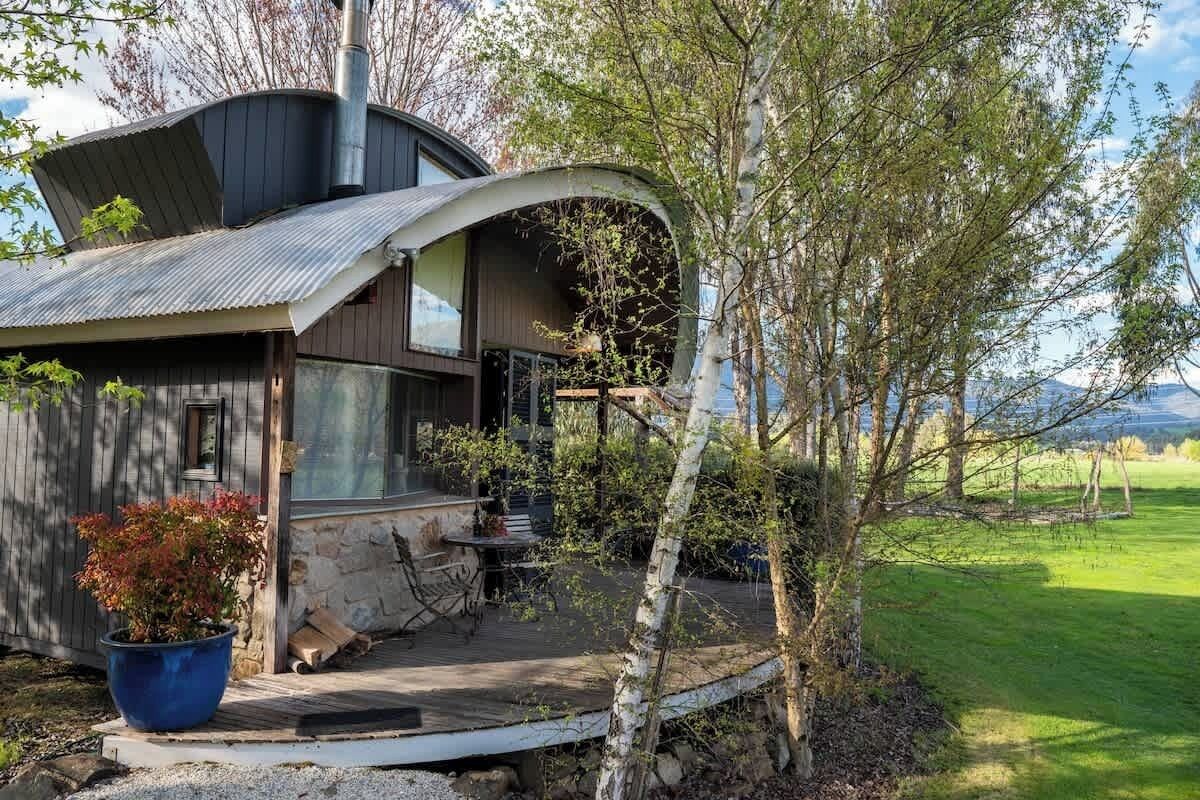 A modern house with a curved roof, a stone foundation, and a wooden deck.