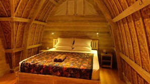 Un dormitorio acogedor en el ático, con techo de madera, una cama con colcha colorida y una mesita de noche pequeña.
