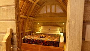 Dormitorio tipo loft con techo inclinado, cama con colcha colorida y suelo de madera.