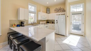 Una cocina moderna con armarios blancos, una isla grande con taburetes de bar, un refrigerador y un microondas.