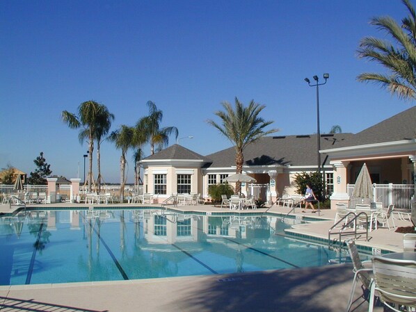 A swimming pool with lounge chairs, palm trees, and a building with a covered patio area.